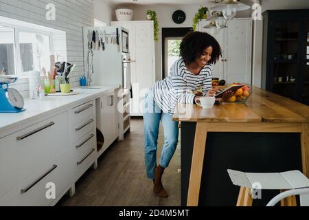 Beautiful mixed race woman with afro browsing tablet in the kitchen at home Stock Photo