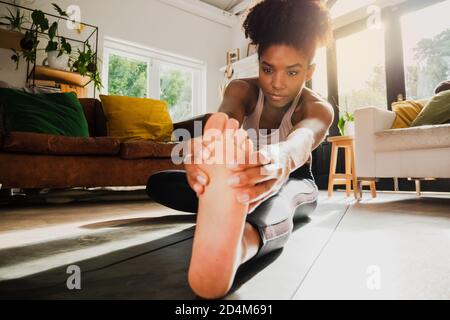 Young female working out from home and stretching legs on yoga mat Stock Photo