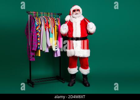 Full length body size view of his he nice fat overweight funny cheerful Santa St Nicholas measuring season clothes hanging on rack choose choice Stock Photo