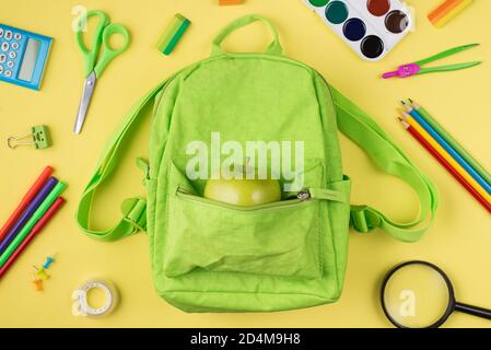 Healthy eating at school concept. Top above overhead view photo of apple green backpack colorful stationery isolated on yellow background Stock Photo