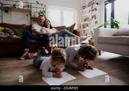 Caucasian family in the living room together, spending quality family time. Kids drawing on the floor while mother and father laugh together Stock Photo