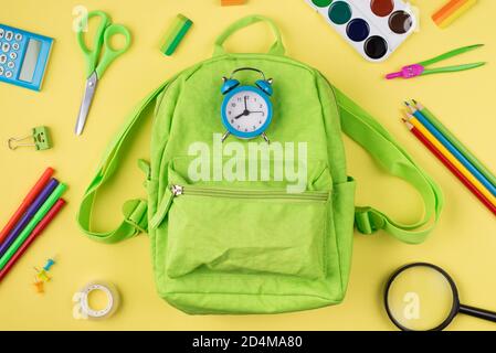 Getting ready for school concept. Top above overhead view photo of blue alarm clock green backpack colorful stationery isolated on yellow background Stock Photo