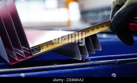 hand using a metal tape measure on sheet metal in close up selective focus shot. industrial background concept. Stock Photo