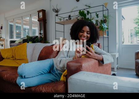 mixed race women happily scrolling through her phone while on the couch. Stock Photo