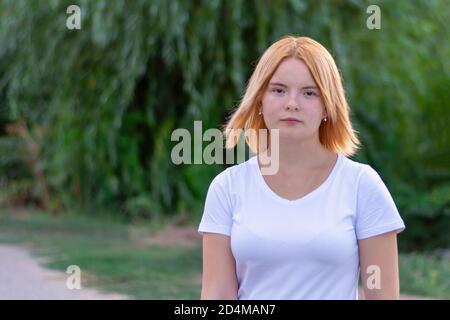 A young woman of blonde Caucasian appearance with brown eyes walks through the park in summer. Close-up, selective focus. Stock Photo