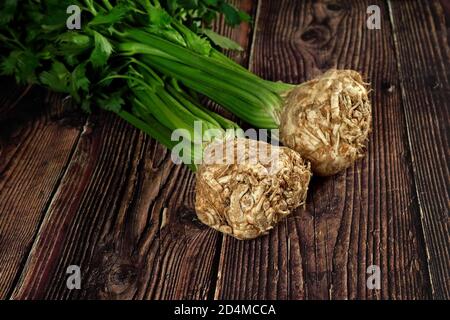 Celeriac root bulbs with green leaves on dark wooden rustic board Stock Photo