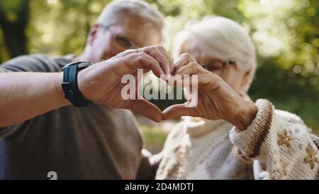 Lovely older retired couple making heart with their hands and looking at each other. Selective focus. High quality photo Stock Photo