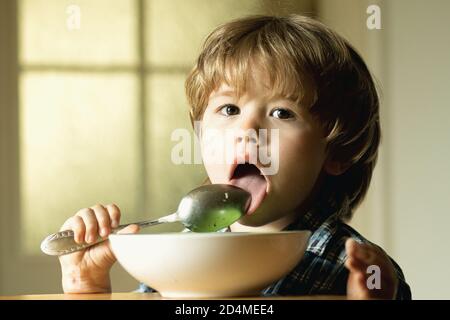 Young kid sitting on the table eating with funny expression on face. Tasty kids breakfast. Tasty kids breakfast. Cheerful baby child eats food itself Stock Photo
