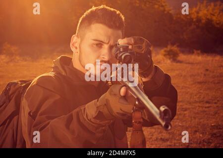 Hunter with Powerful Rifle with Scope Spotting Animals. Rifle Hunter Silhouetted in Beautiful Sunset. Autumn hunting season. Stock Photo