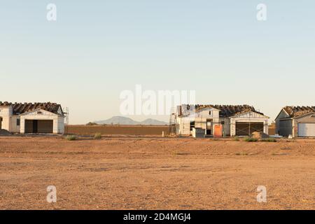 A row of houses being constructed on a dirt lot with an empty lot between and view of the mountains in background stands in central Arizona building boom. Stock Photo