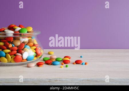 Multi-colored candies. Round candies  in a glass jar on a white table. Lilac background Stock Photo