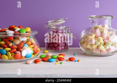 Multi-colored sweets. Candies in glass jars on a white table. Lilac background Stock Photo