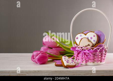 Gingerbread cookies and tulips. Gingerbread in the shape of a heart in a wicker basket and a bouquet of tulips. Gray background Stock Photo