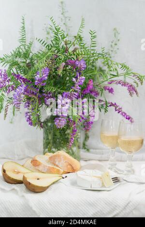 Violet flowers, pears, bri cheese and wine glasses. French style still life. Vertical orientation Stock Photo