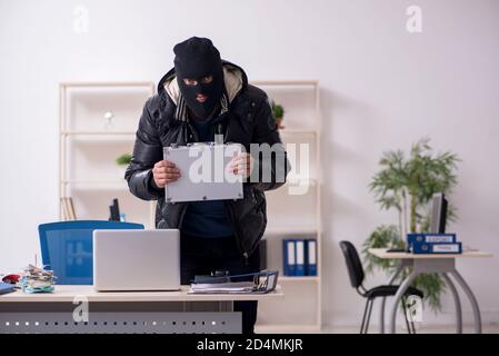 Young male burglar in the office room Stock Photo
