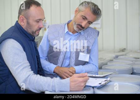 manager noting on clipboard and worker taping box in warehouse Stock Photo