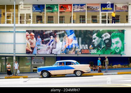 Old classic car next to a billboard with revolutionary slogans in Havana Stock Photo