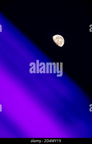 Gibbous moon against clear black skies, with colorful blue and purple blurred planetlike horizon in forgeround Stock Photo