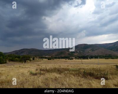 Cloudy sky, green mountains, dry grasses, path and trees. A rural ...