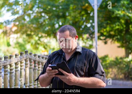 Caucasian man on the street of another city looks into a smartphone and looks for a way through a map in the phone. Stock Photo