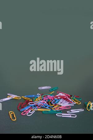 Multicolored paper clips lie on a plain green background. Close up. Vertical format Stock Photo