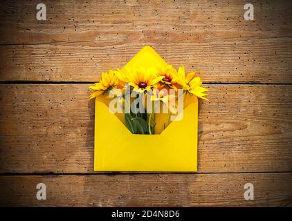 Yellow paper envelope with rudbeckia or black-eyed susan garden flowers on old wooden boards background. Rustic style. Festive floral template. Greeti Stock Photo