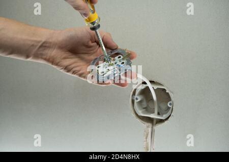 Close up of technician holding screwdriver near power socket. Electrician connects the sockets to the electrical wires. Installation wire into a plug. Stock Photo