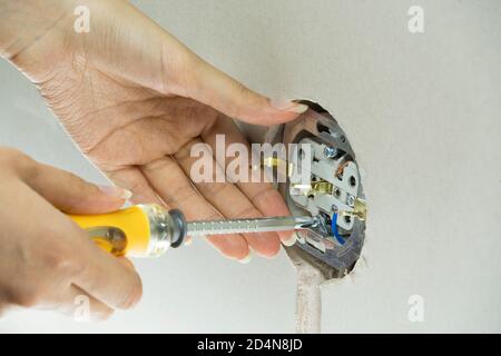 Woman repairs an electric socket with a screwdriver. Installing new socket into the wall. Installation wire into a plug. Holding screwdriver near sock Stock Photo