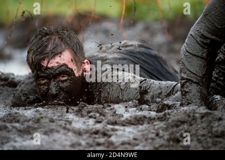 Mud race runners. Crawling,passing under a barbed wire obstacles during extreme obstacle race. Extreame sport concept Stock Photo