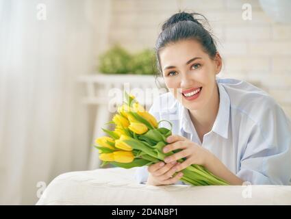 Beautiful young woman in the blue dress with flowers tulips in hands on bed at home. Stock Photo