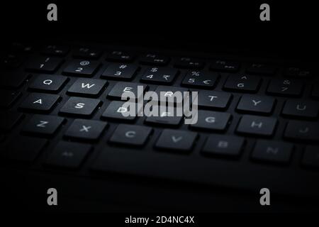 Closeup of black laptop QWERTY keyboard with light falling on keys. Stock Photo