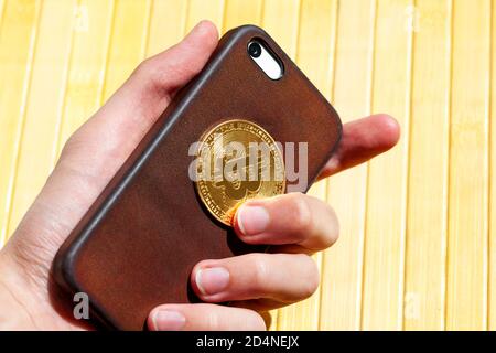 Hand holding a modern smartphone and a golden bitcoin coin symbol. E-commerce, earning with mobile crypto currency trading apps, phone bit wallet Stock Photo