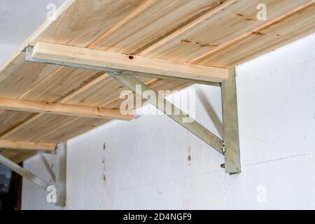 Close-up of a wooden shelf supported by a triangular iron frame on the wall Stock Photo