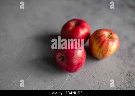 Three Ripe garden red apples on gray concrete. Fruits concept of the fall harvest. Space for text. Selective soft focus. Stock Photo