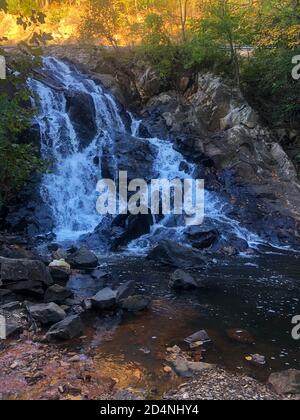 Sun sets behind a waterfall, autumn foliage and black rocks. Stock Photo