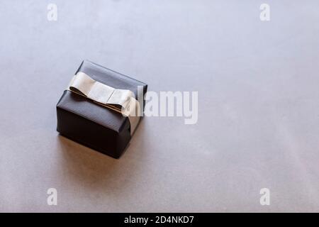 A  gift wrapped in black wrapping paper with a brown bow laying on a grey surface. Minimalistic present for a man during festive season or Christmas Stock Photo