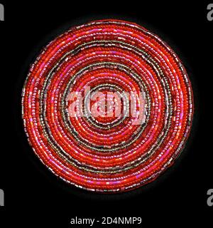 Macro image of a circular pink beaded coaster with small, glass iridescent beads sewn in concentric circles, isolated on a black background. Stock Photo