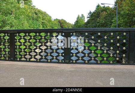 Ornate iron trellis fencing on a pedestrian footpath which is bridging a tree lined road. Stock Photo