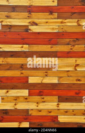 Panelled wall created with rustic, knotted wooden slats in an array of autumnal colours. Stock Photo