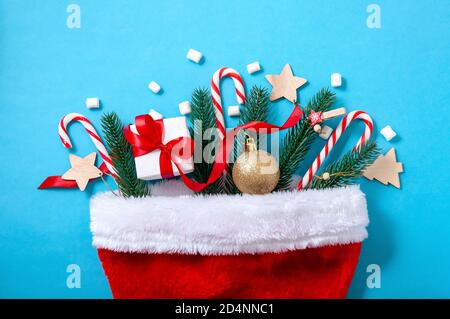 Creative Christmas Concept with Santa Hat, Fir Tree, Gift Box, Ball and Candys on Blue Background. Top View. Flat Lay. Stock Photo