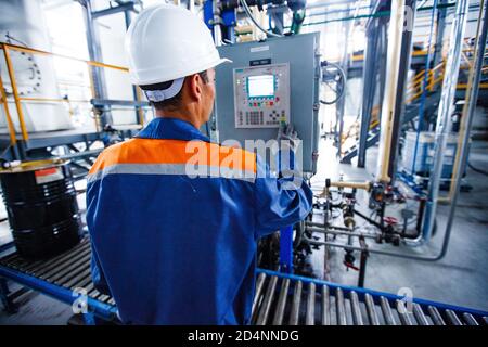 Shymkent, Kazakhstan - April 26 2012: Motor oil modern production plant. Operator worker and control panel in factory workshop. Pipes on background. Stock Photo