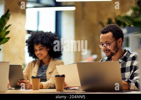 Using modern technologies. Two young multiracial business people sitting at the desk, working together in coworking space. Office life, teamwork and business Stock Photo
