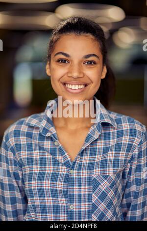 Vertical shot of a young happy mixed race business woman in casual wear looking at camera and smiling while posing in the office. Business people concept Stock Photo