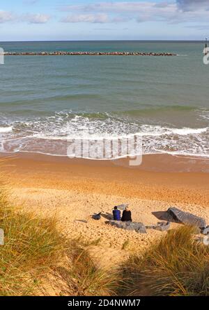 A couple sitting on a rock looking out to sea from a beach on the Norfolk coast at Sea Palling, Norfolk, England, United Kingdom. Stock Photo
