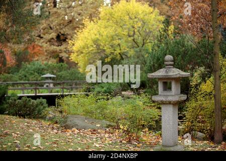 Stone Japanese lantern and bridge across the pond in the autumn day in the Main Botanical garden of the Academy of Sciences of Russia, Japanese garden Stock Photo