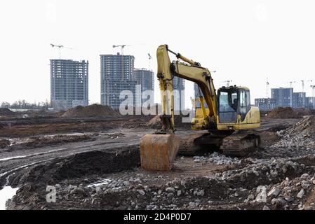 Yellow excavator with bucket at building under construction. Backhoe at large scale construction site against tower cranes. Digging the ground for the Stock Photo