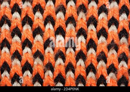 Synthetic knitted fabric with pattern elements of red, black and white yarns close up. Multicolor patterned knitted fabric texture. Background Stock Photo