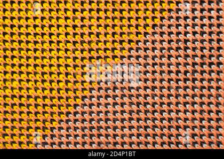 Synthetic knitted fabric with pattern elements of yellow, black, white and red yarns close up. Multicolor patterned knitted fabric texture. Diagonal p Stock Photo