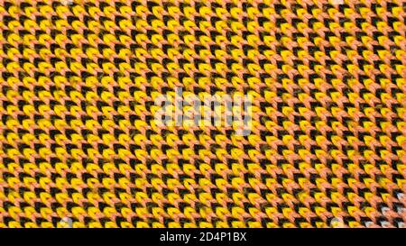 Synthetic knitted fabric with pattern elements of yellow, black and red yarns close up. Multicolor patterned knitted fabric texture. Background Stock Photo