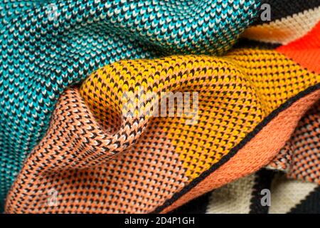 A pile of multi-colored synthetic knitted fabrics of different structures and textures. A stack of colorful fabrics smooth shapes background. Multicol Stock Photo